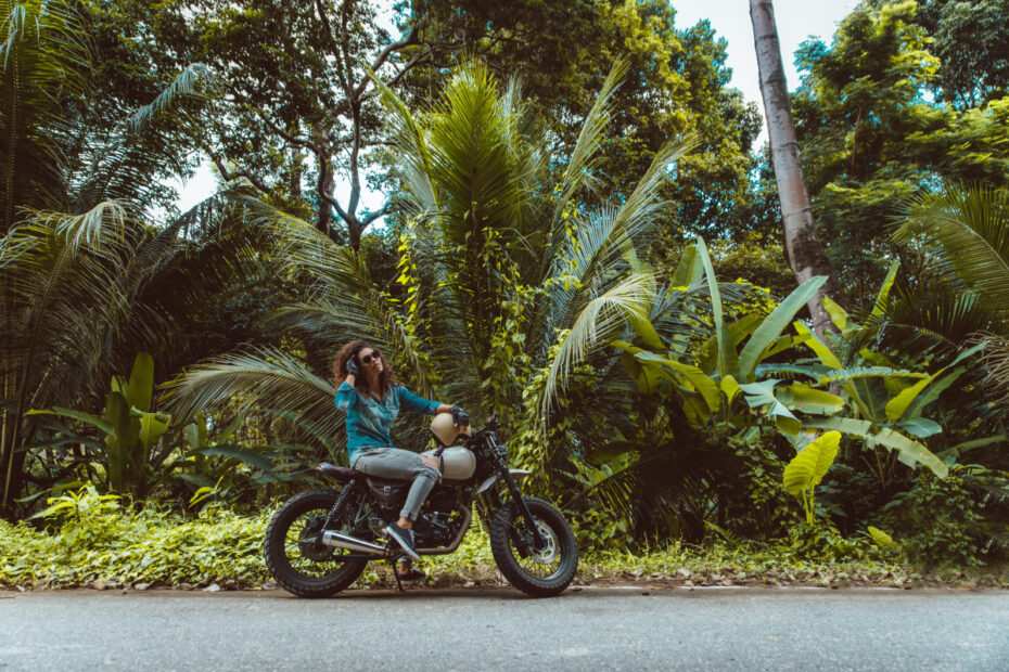 Une voyageuse à moto sur une route sinueuse au cœur d'une forêt tropicale luxuriante en Indonésie.